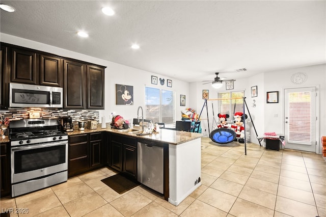 kitchen featuring light stone counters, a peninsula, light tile patterned flooring, a sink, and stainless steel appliances