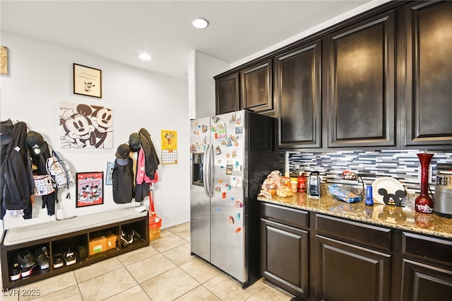 kitchen with tasteful backsplash, dark brown cabinets, stainless steel fridge with ice dispenser, light tile patterned floors, and light stone counters