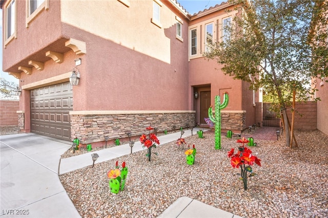 view of property exterior with stucco siding, driveway, stone siding, fence, and an attached garage