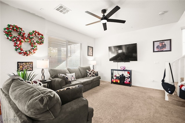 carpeted living room with visible vents, stairs, and a ceiling fan