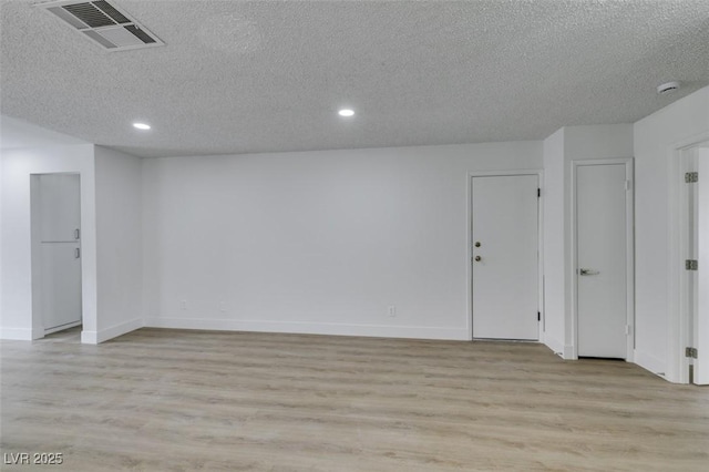 unfurnished room featuring light wood-style flooring, baseboards, visible vents, and a textured ceiling