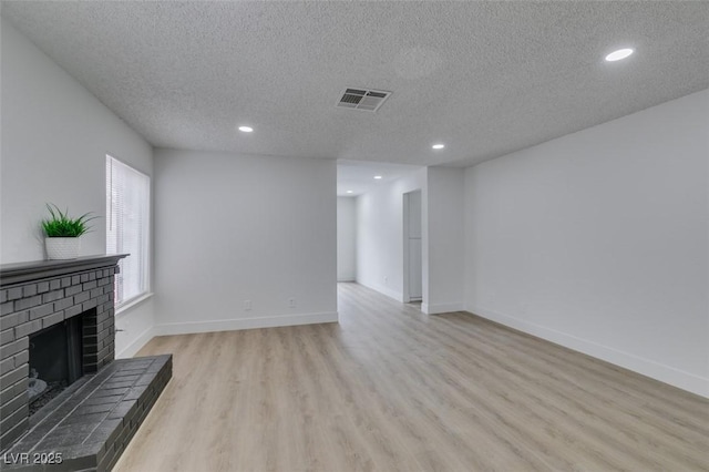 unfurnished living room with visible vents, a brick fireplace, baseboards, and light wood-style floors