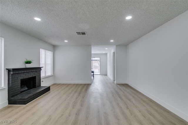 unfurnished living room with visible vents, baseboards, a fireplace, light wood-style floors, and a textured ceiling