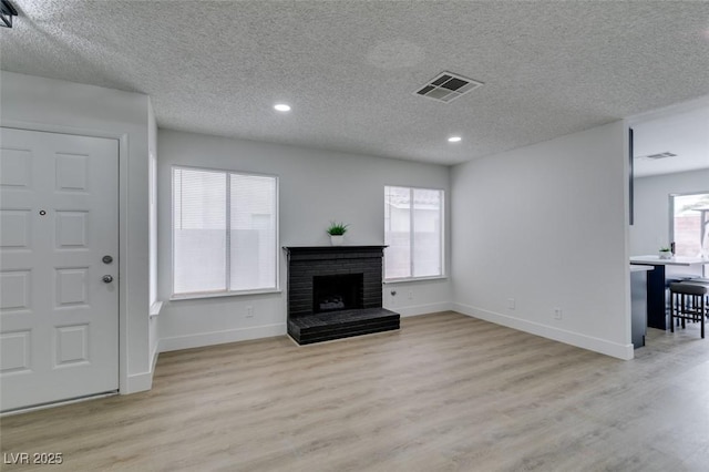 unfurnished living room with a brick fireplace, visible vents, light wood-type flooring, and baseboards