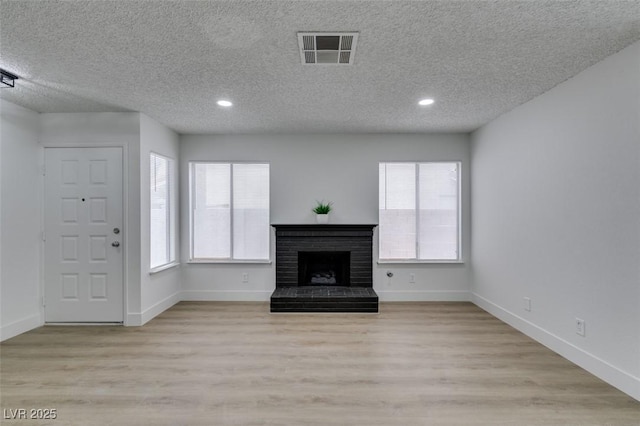 unfurnished living room featuring visible vents, plenty of natural light, a brick fireplace, and wood finished floors