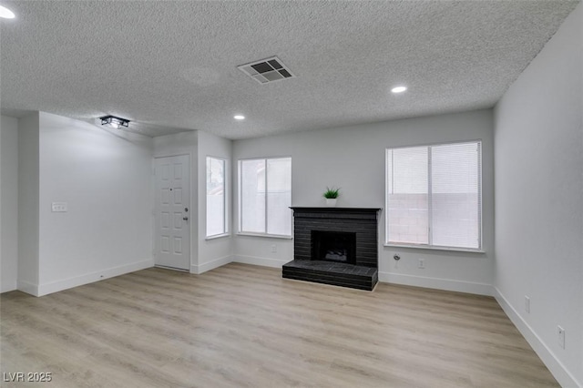 unfurnished living room featuring a brick fireplace, baseboards, visible vents, and light wood finished floors