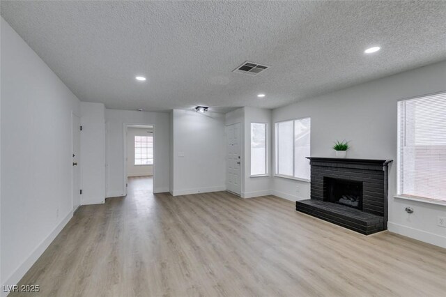 unfurnished living room featuring a brick fireplace, light wood-style floors, visible vents, and baseboards