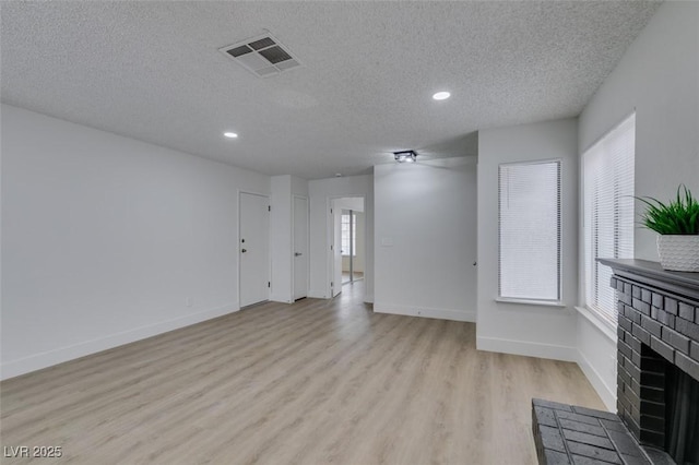 unfurnished living room with visible vents, a textured ceiling, light wood finished floors, baseboards, and a brick fireplace