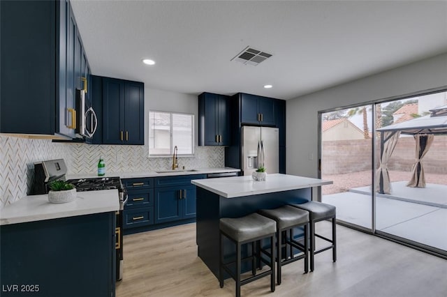 kitchen with visible vents, a sink, stainless steel appliances, a kitchen bar, and blue cabinets