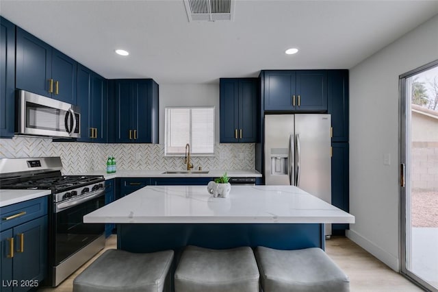 kitchen featuring visible vents, a kitchen bar, appliances with stainless steel finishes, blue cabinets, and a sink