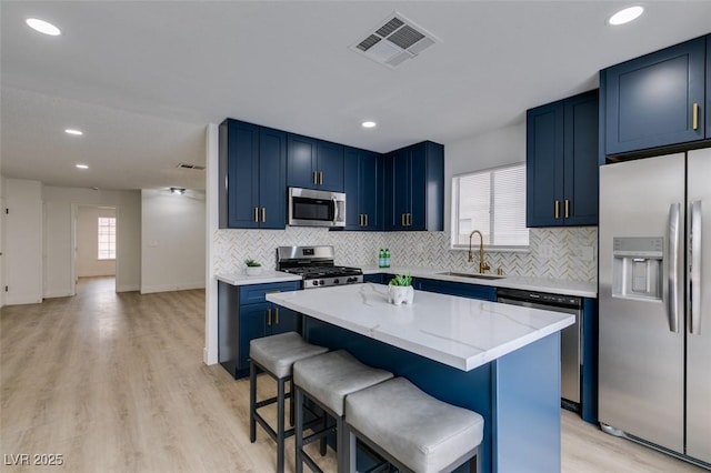 kitchen with visible vents, blue cabinetry, a sink, stainless steel appliances, and a kitchen bar