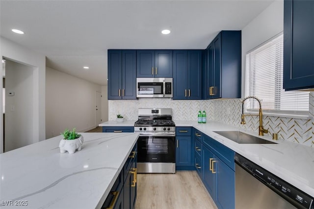 kitchen with blue cabinetry, light stone countertops, decorative backsplash, stainless steel appliances, and a sink