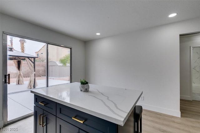 kitchen with light stone counters, a center island, recessed lighting, light wood finished floors, and baseboards