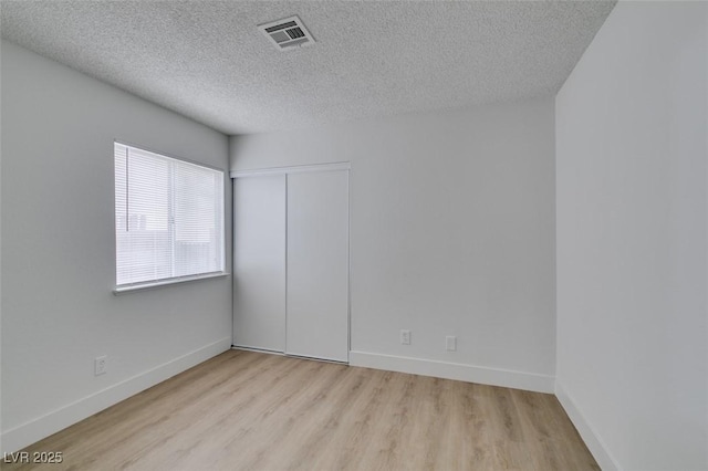 spare room featuring visible vents, a textured ceiling, baseboards, and wood finished floors