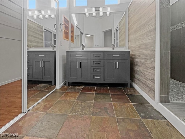 bathroom with a walk in shower, a sink, stone tile flooring, a high ceiling, and double vanity