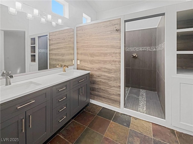 full bathroom featuring double vanity, stone tile floors, a walk in shower, and a sink