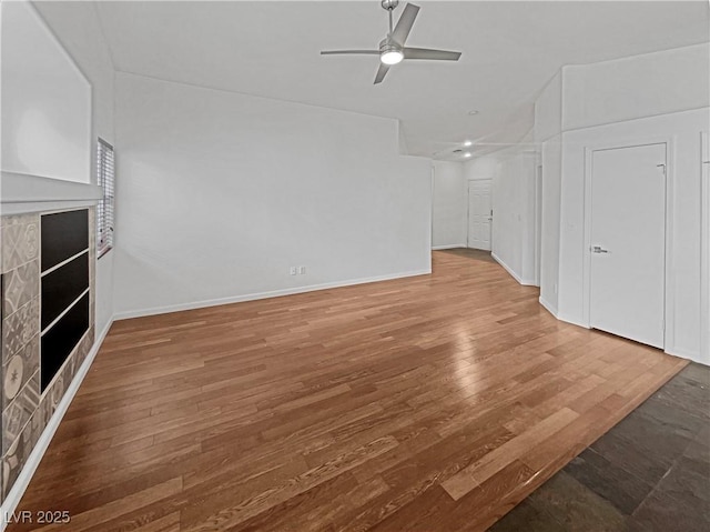 unfurnished living room with a fireplace, baseboards, ceiling fan, and wood finished floors