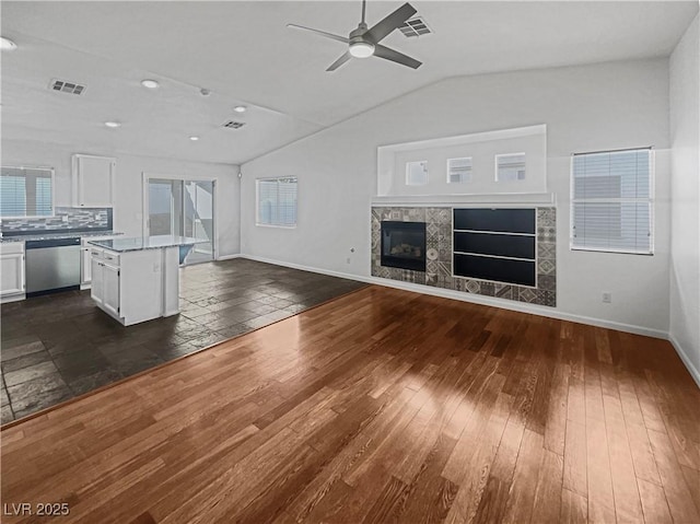 unfurnished living room featuring baseboards, visible vents, dark wood finished floors, a tile fireplace, and vaulted ceiling