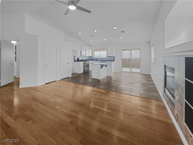 unfurnished living room featuring dark wood finished floors, visible vents, a tile fireplace, and lofted ceiling