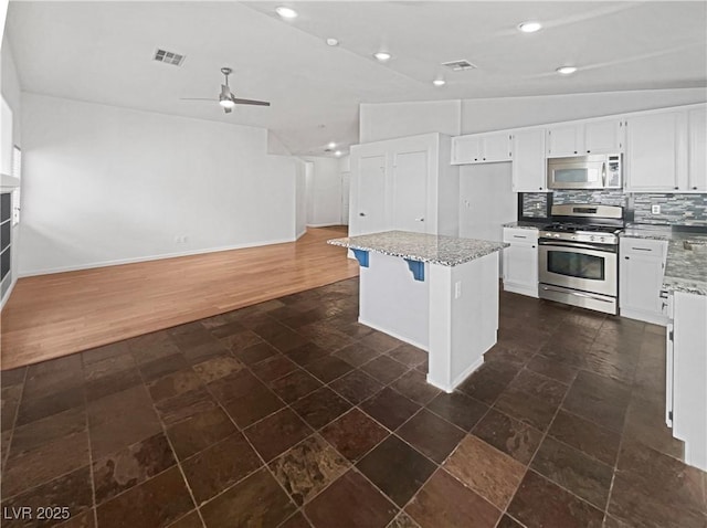 kitchen with visible vents, a kitchen island, light stone countertops, decorative backsplash, and appliances with stainless steel finishes