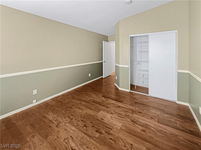 unfurnished bedroom with a closet, baseboards, wood finished floors, and vaulted ceiling