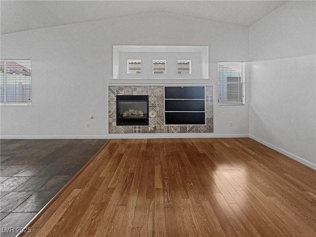 unfurnished living room featuring a tile fireplace, wood-type flooring, baseboards, and vaulted ceiling