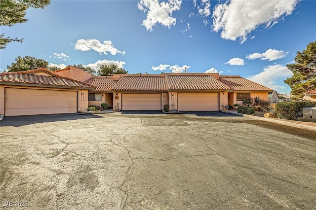 view of front of house with stucco siding, driveway, an attached garage, and a tiled roof