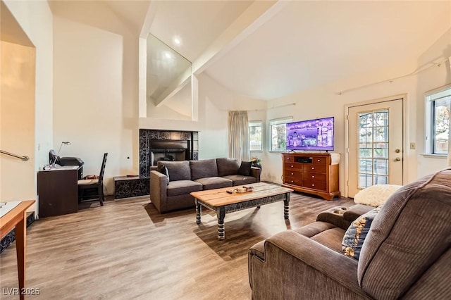 living room featuring a high end fireplace, beamed ceiling, plenty of natural light, and light wood finished floors