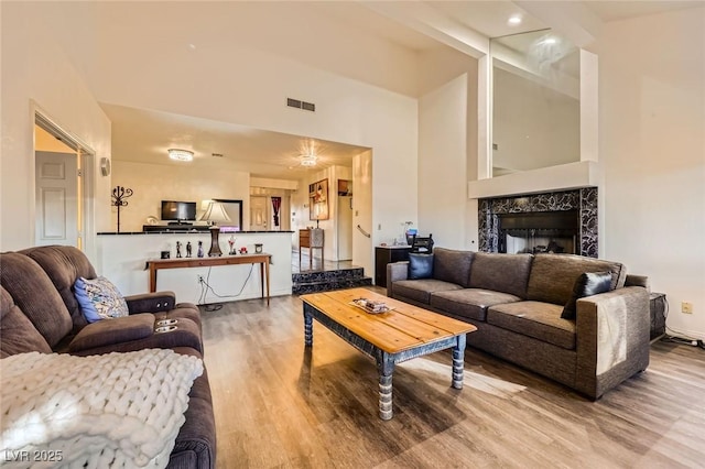 living area with visible vents, a fireplace, a towering ceiling, and wood finished floors