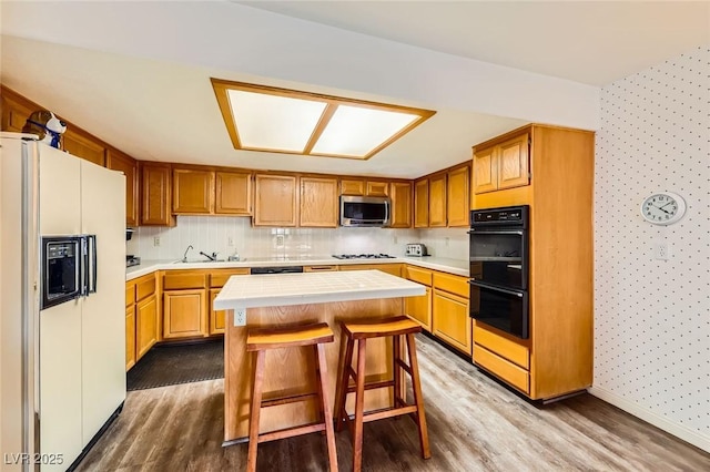 kitchen with dobule oven black, stainless steel microwave, gas cooktop, a kitchen island, and white refrigerator with ice dispenser