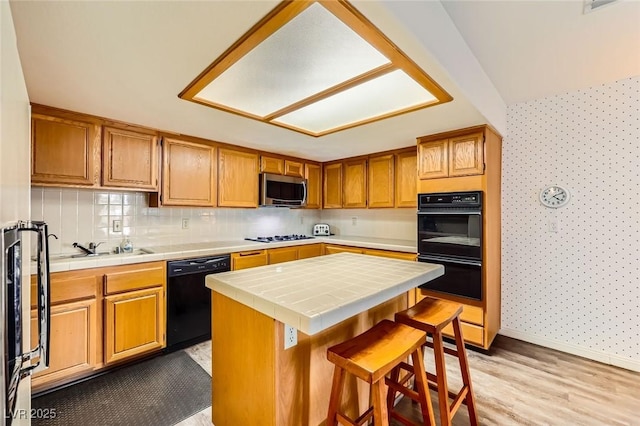 kitchen with a center island, tile countertops, light wood-type flooring, a kitchen breakfast bar, and black appliances