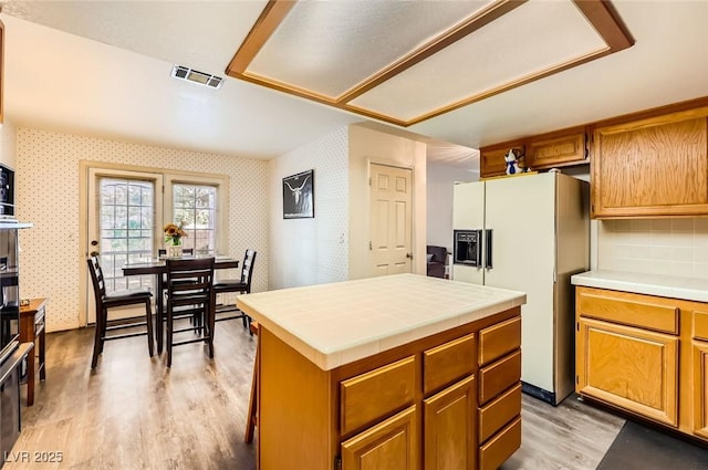 kitchen featuring visible vents, wallpapered walls, white refrigerator with ice dispenser, light wood finished floors, and tile counters