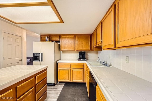 kitchen with tile countertops, a sink, decorative backsplash, white refrigerator with ice dispenser, and brown cabinets