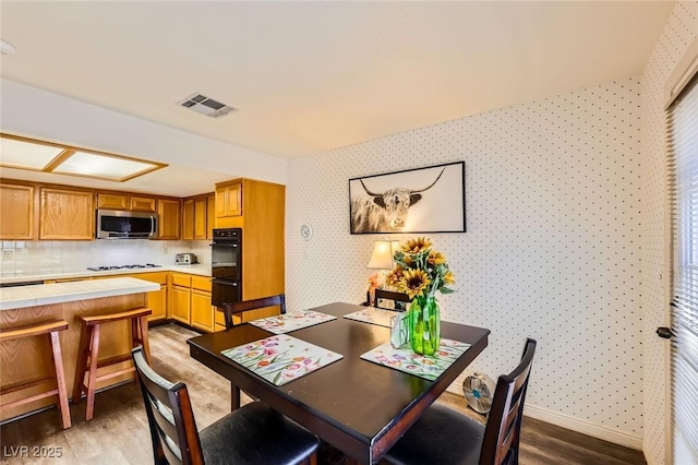 dining space featuring wallpapered walls, light wood-style flooring, baseboards, and visible vents