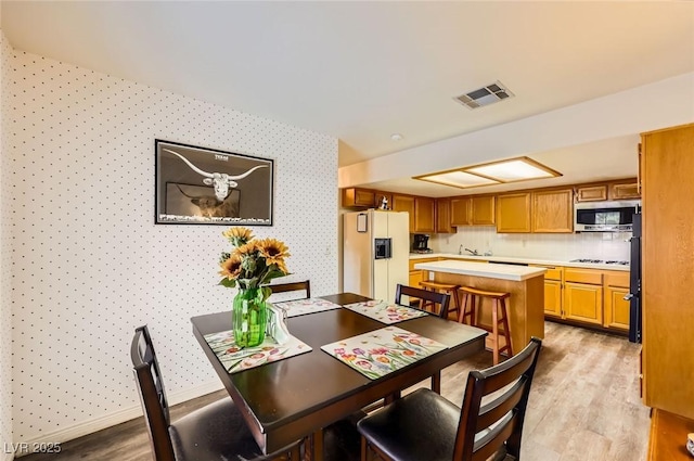 dining area featuring light wood-type flooring, visible vents, wallpapered walls, baseboards, and attic access