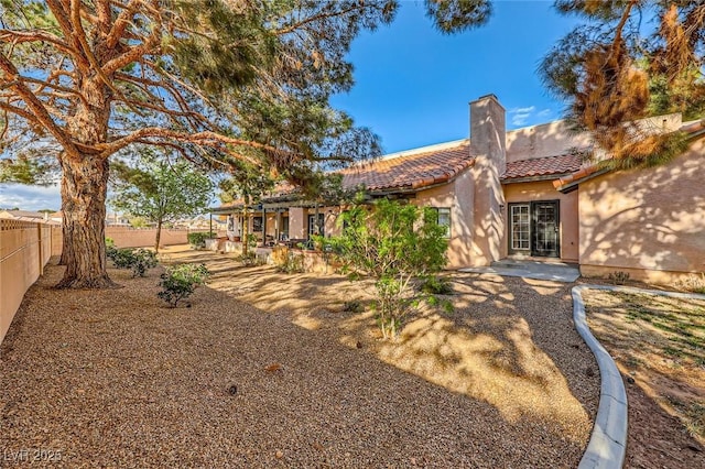 exterior space featuring fence, a tile roof, stucco siding, a chimney, and a patio