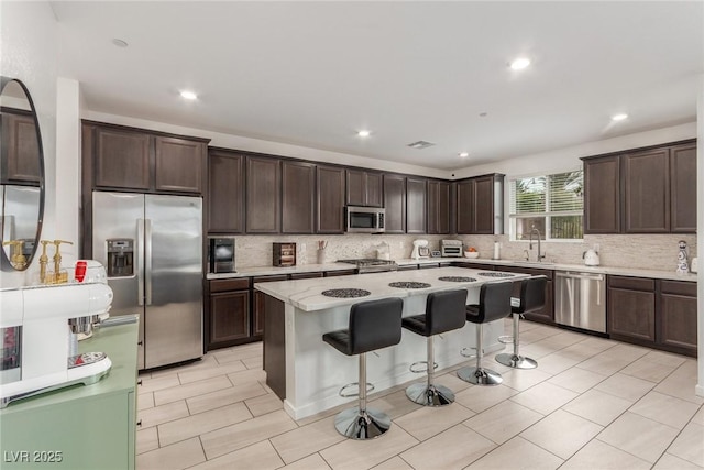 kitchen with stainless steel appliances, dark brown cabinetry, a kitchen bar, backsplash, and a center island