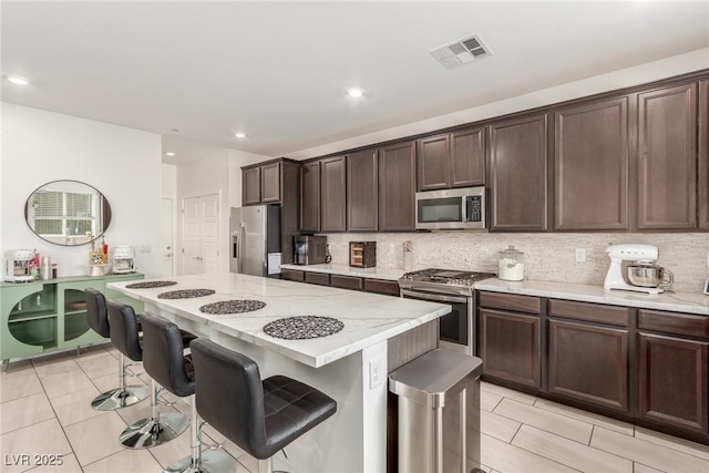 kitchen with visible vents, a kitchen island, tasteful backsplash, appliances with stainless steel finishes, and a breakfast bar area