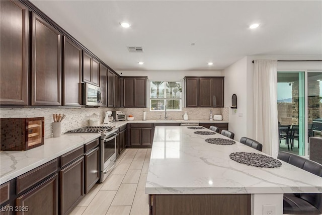 kitchen with a kitchen bar, decorative backsplash, appliances with stainless steel finishes, and a kitchen island