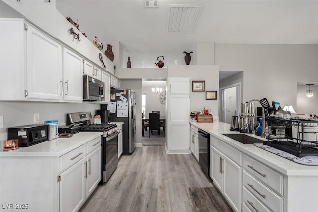 kitchen featuring a peninsula, light countertops, appliances with stainless steel finishes, white cabinetry, and light wood-type flooring