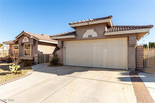 mediterranean / spanish-style house with stucco siding, a tile roof, a gate, concrete driveway, and an attached garage