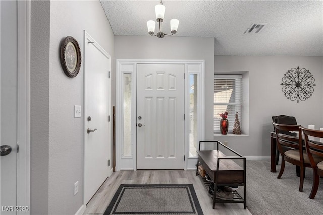 foyer with baseboards, a textured ceiling, a chandelier, and light wood finished floors