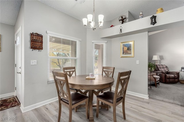 dining room with a notable chandelier, a textured ceiling, light wood-style floors, and vaulted ceiling