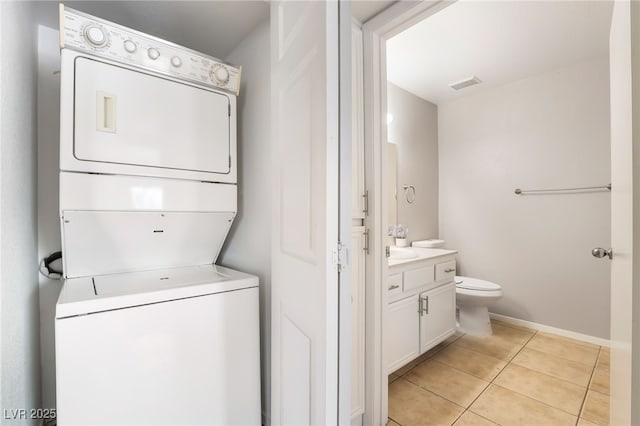 clothes washing area with light tile patterned floors, baseboards, visible vents, stacked washing maching and dryer, and laundry area