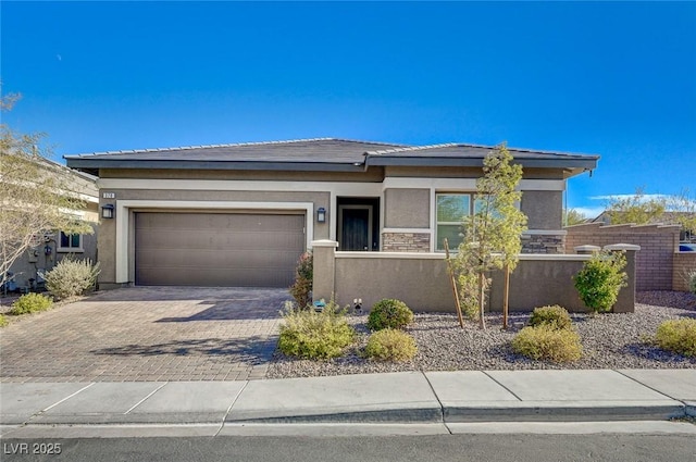 prairie-style house with stucco siding, stone siding, a garage, a fenced front yard, and decorative driveway