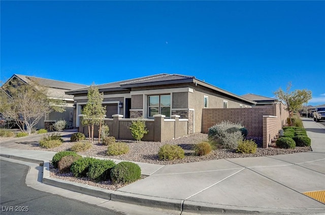 view of front of home with stucco siding, driveway, a fenced front yard, a garage, and brick siding