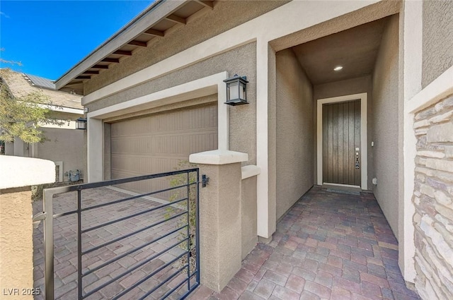 property entrance with a gate, an attached garage, and stucco siding