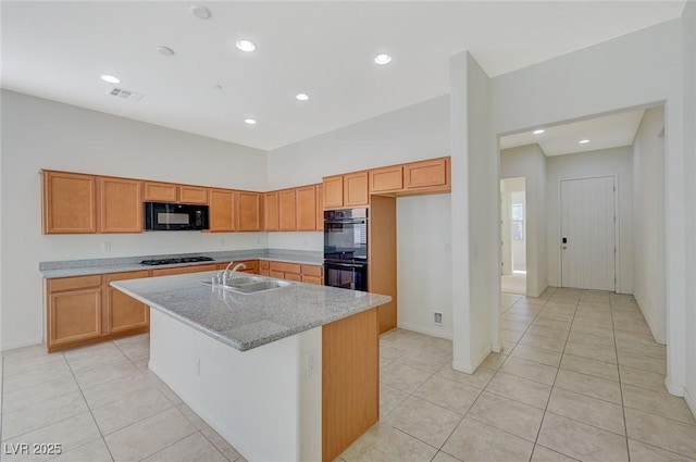 kitchen with light tile patterned floors, visible vents, an island with sink, a sink, and black appliances