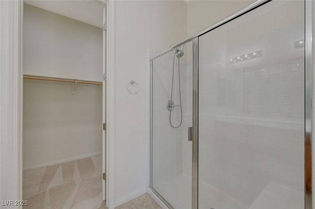 full bath featuring a walk in closet, baseboards, and a stall shower