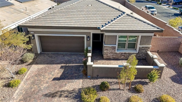 view of front facade featuring fence, an attached garage, stucco siding, stone siding, and decorative driveway